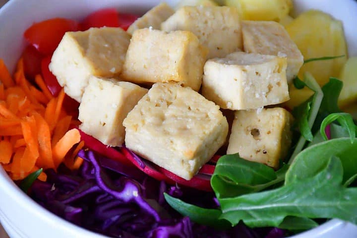 Un bol de poke au tofu cuit au four coloré et rempli de fruits et de légumes.