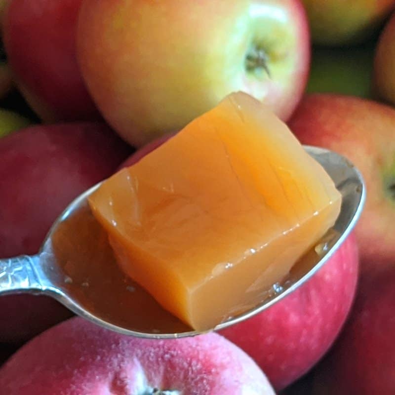 A square of apple jello in a spoon over a box of apples.