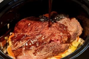 Pouring the broth over the beef roast in the slow cooker.