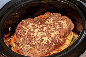 Seasoning the beef roast with pepper and garlic in the slow cooker.