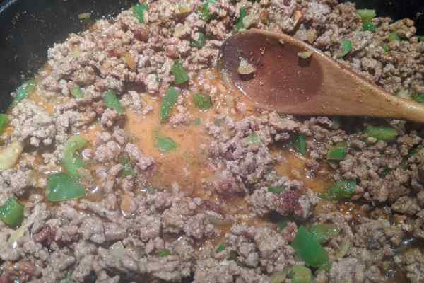 Ground beef and diced green pepper bell cooking in a cast iron skillet to make a delicious low sodium meat mix for burritos and tacos.