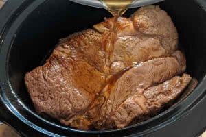 Pouring broth on the roast beef in the slow cooker.