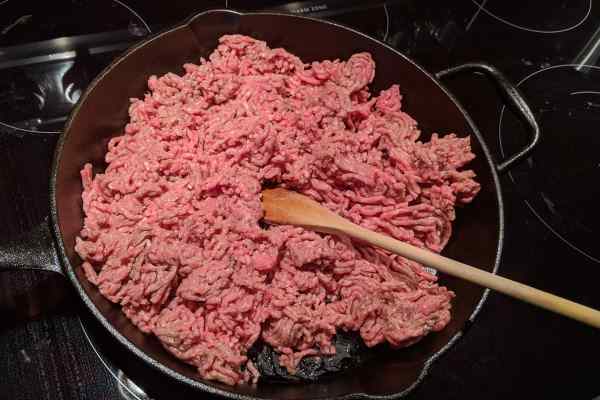 Raw ground beef cooking in a cast iron skillet.