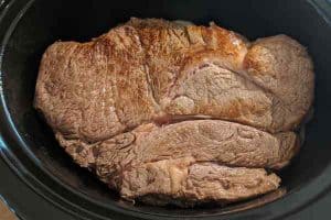 Roast beef placed in the slow cooker over a layer of sliced onions.