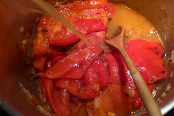Adding the unsalted broth and roasted red peppers to the soup.