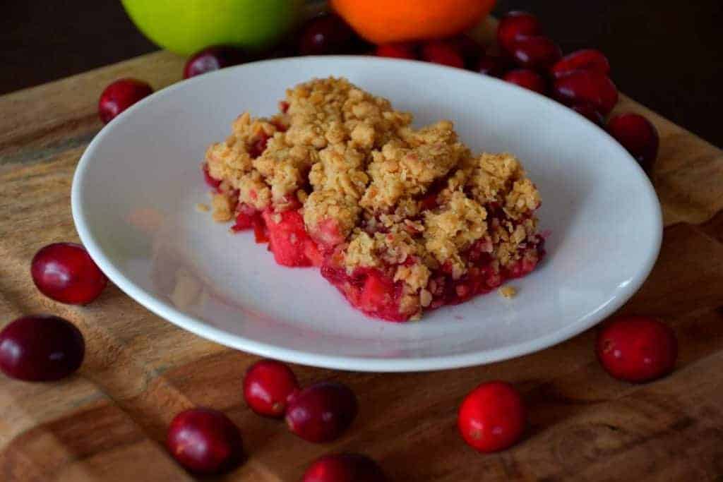 A kidney healthy apple cranberry crumble recipe on a wooden board with fresh cranberries.