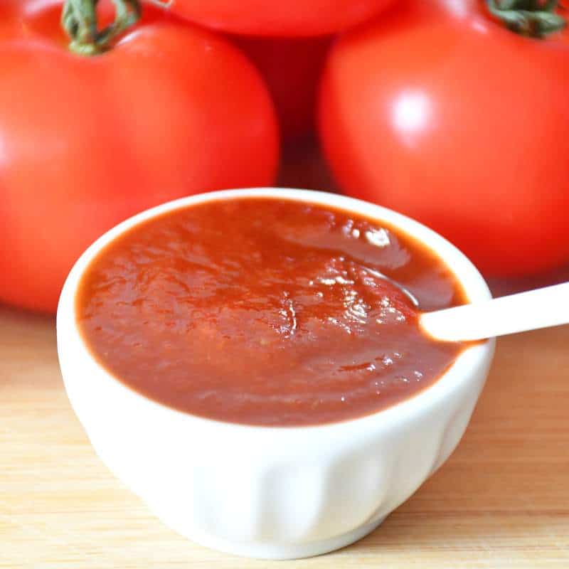 Présentation de la recette de ketchup maison simple sans sel avec un arrière plan de tomates.