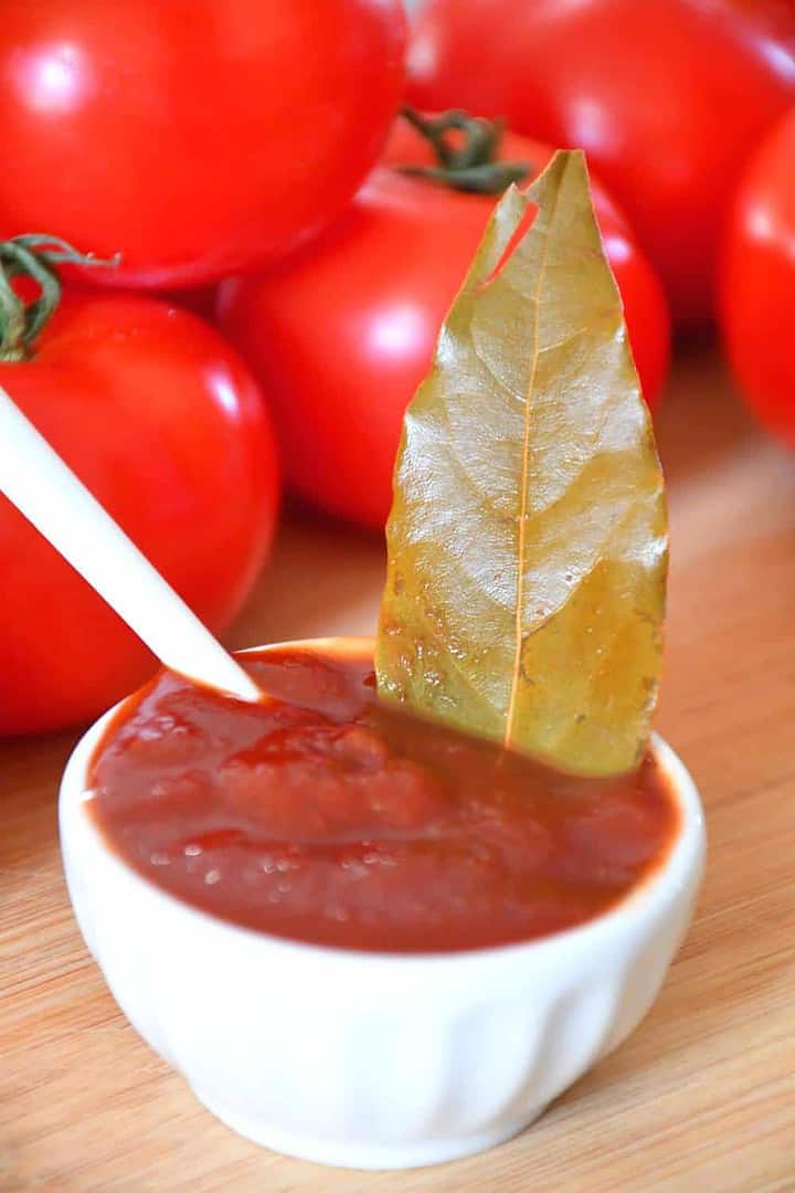 salt free simple homemade chipotle and laurel ketchup presentation with tomatoes background.