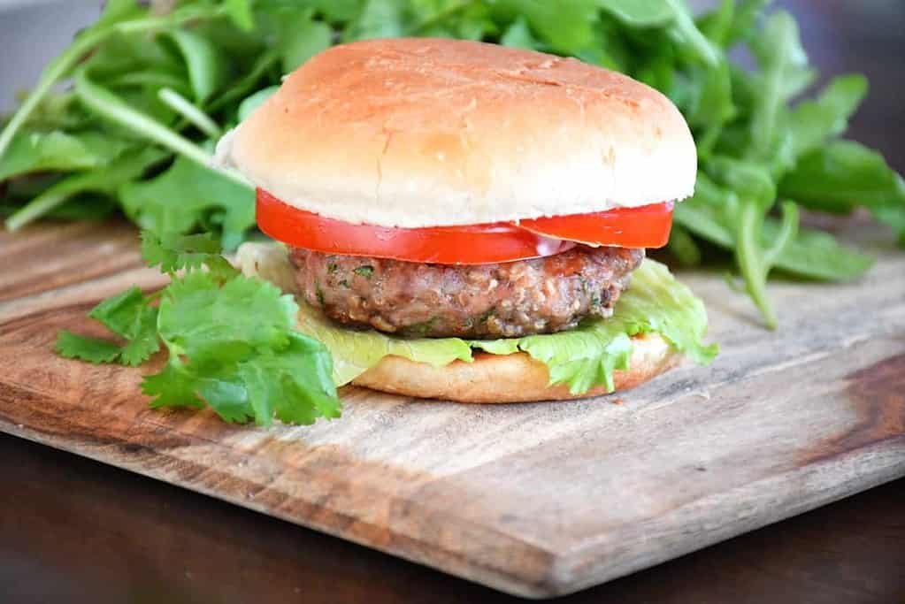 Assembled cilantro pork burger on a wooden board served with green salad.