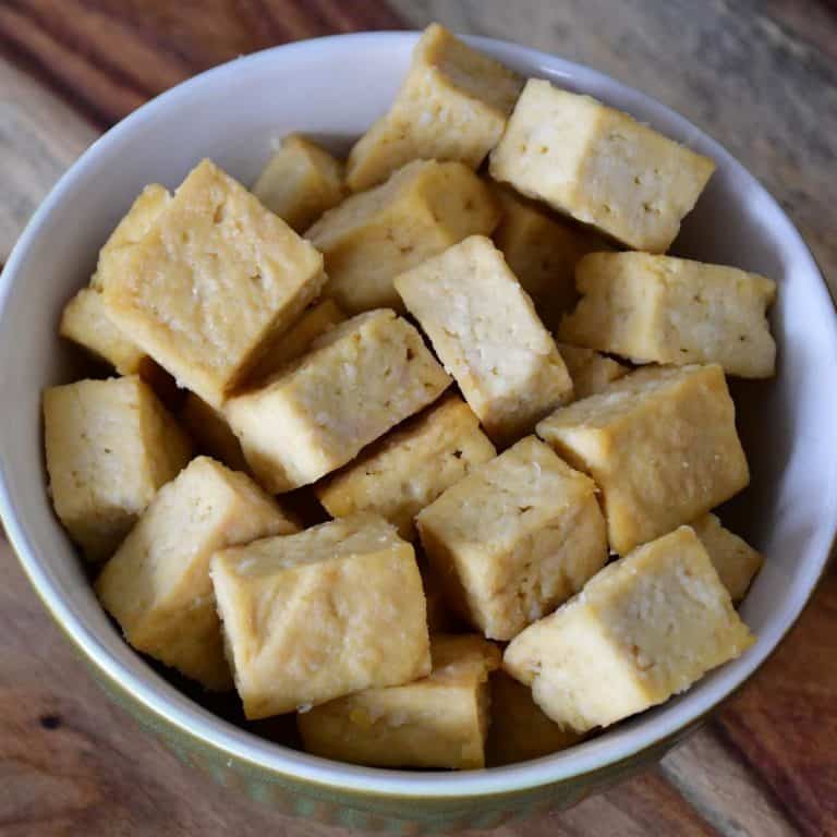 A close-up on baked tofu cubes in a classic green bowl.