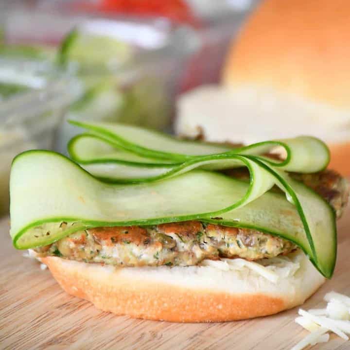 Assembly of cilantro pork burger with cucumber slices and grated Swiss cheese.