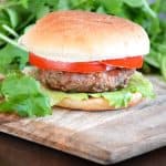 Featured cilantro pork burger on a wooden board served with a healthy green salad.