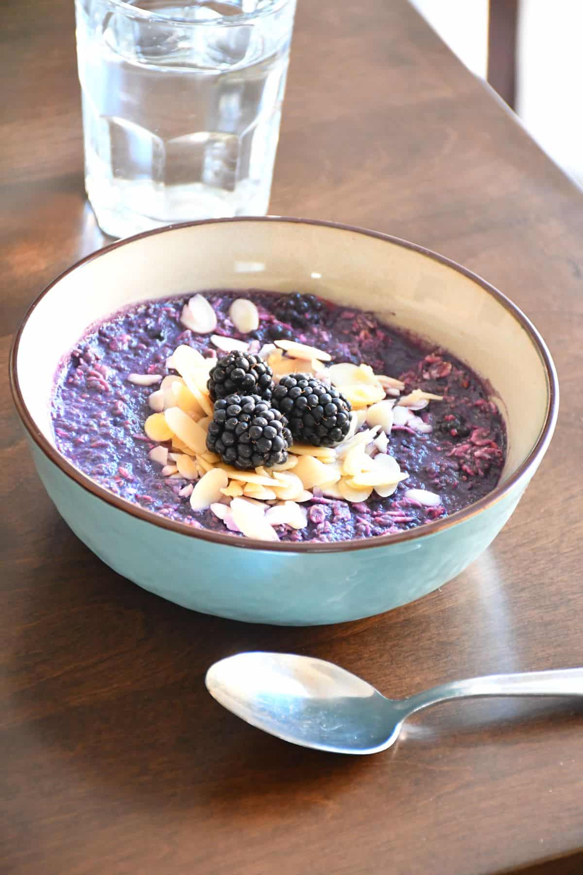 A double blackberry overnight oatmeal topped with sliced almonds and fresh blackberries featured in a blue ceramic bowl.