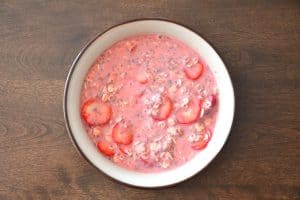Combining all the basic ingredients to make a double strawberry overnight oatmeal in a bowl.