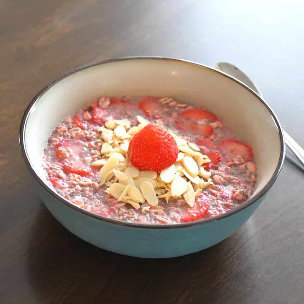 A close-up on the final result of the double strawberry overnight oats topped with sliced almonds and a fresh strawberry in a blue ceramic bowl.