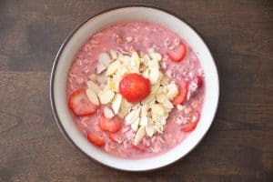 Sliced almonds and a fresh strawberry added on top of a double strawberry overnight oatmeal.