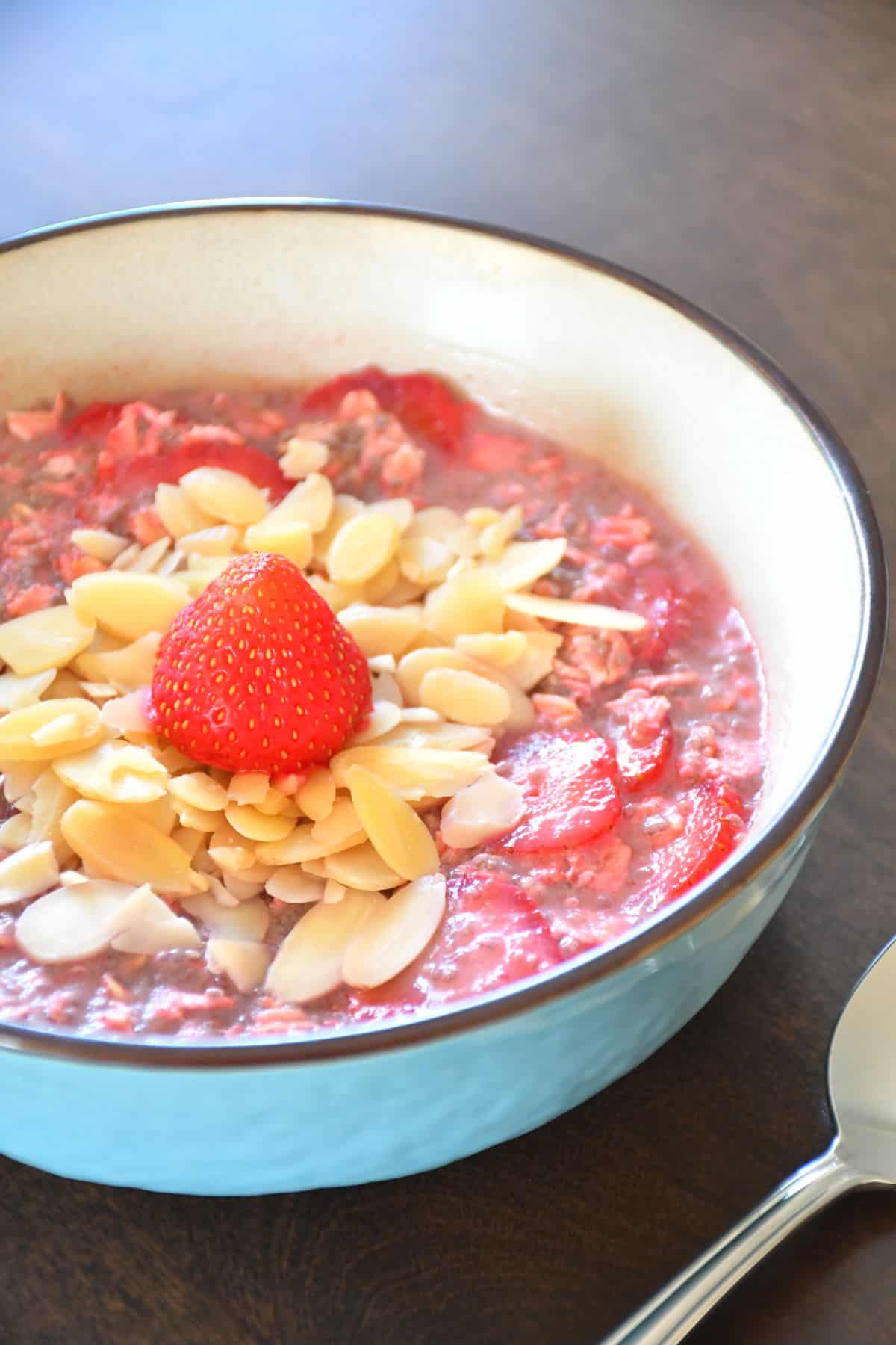 A delicious double strawberry overnight oatmeal in a blue ceramic bowl and a spoon on a wooden table.