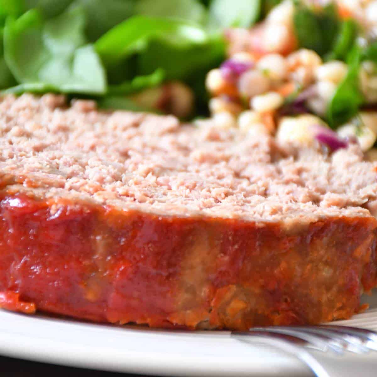 A close-up on a low sodium meatloaf slice served with greens.