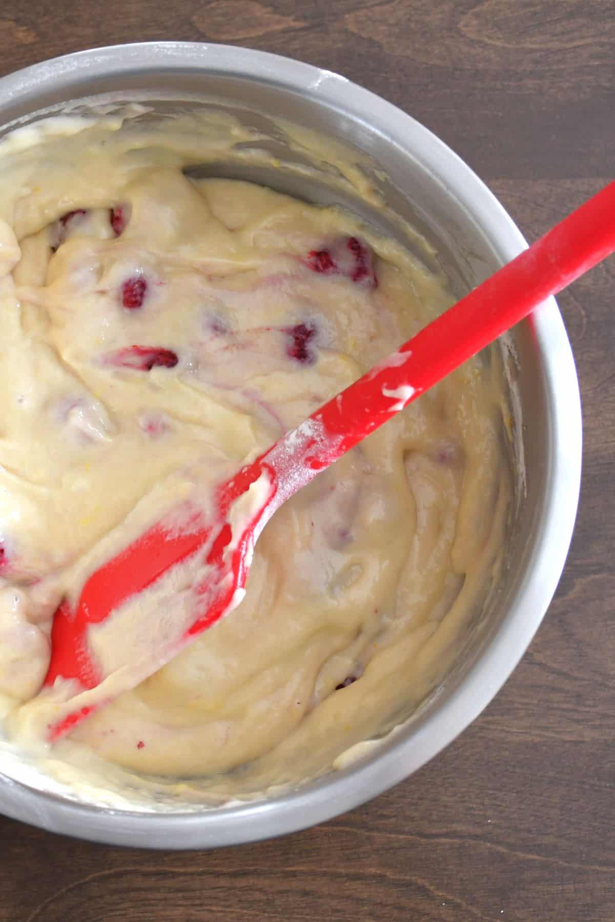 Mixing raspberries in the lemon raspberry batter without coloring it in a stainless mixing bowl.