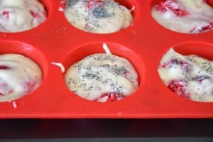 Ajouter des graines de pavot sur le dessus de la pâte à muffins citron framboise dans un moule en silicone rouge.